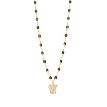 A gold chain necklace featuring small dark beads and a gold sea turtle pendant adorned with clear stones, shown against a plain white background.
