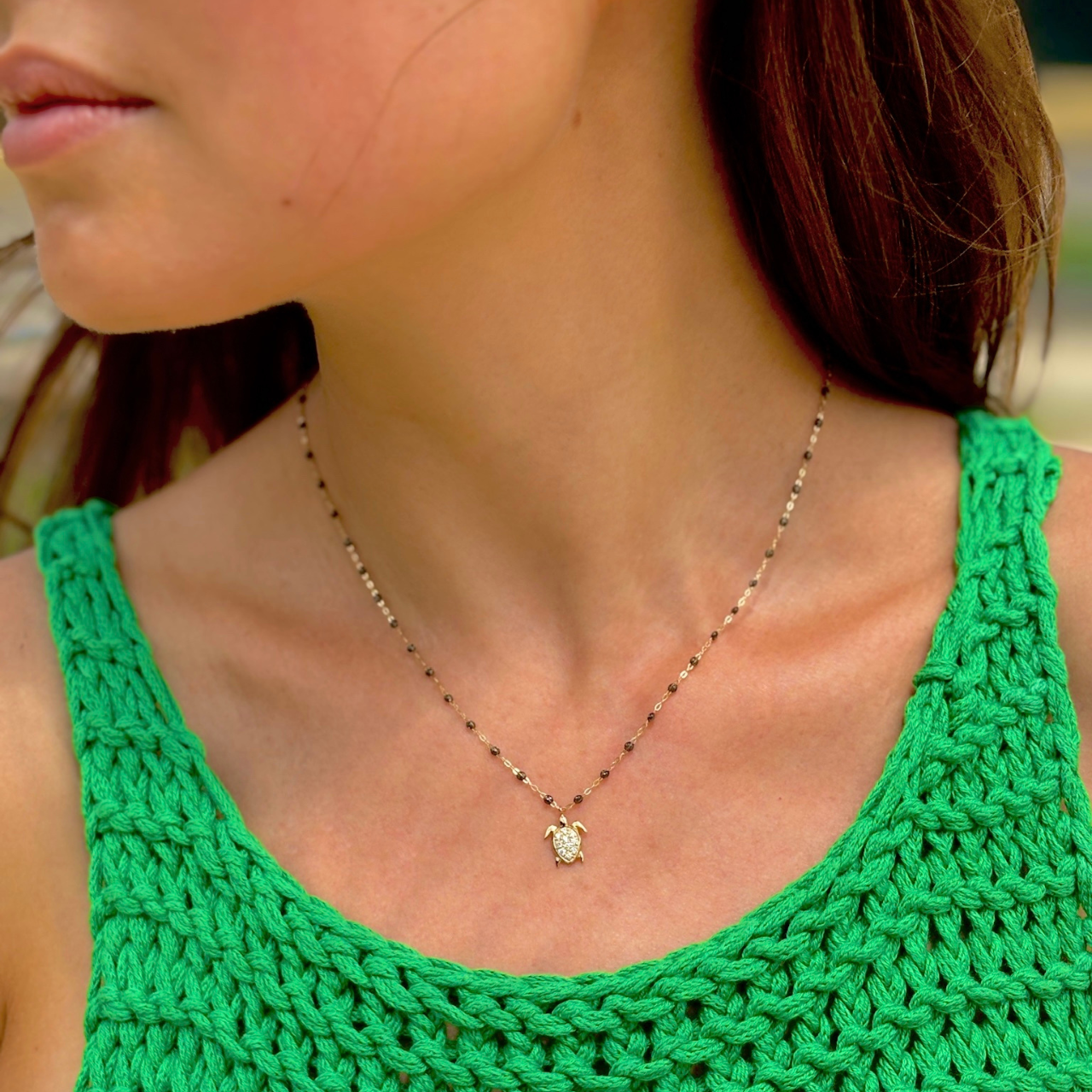 A gold chain necklace featuring small dark beads and a gold sea turtle pendant adorned with clear stones, shown against a plain white background.